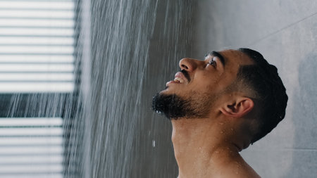 Portrait young handsome manly wet man bearded brunette guy washes in shower enjoys falling water flowing over male face washing hair refreshed after workout in gym morning hygieneの写真素材