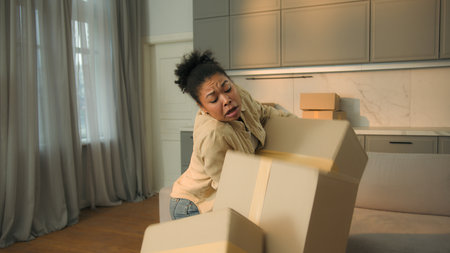Female homeowner African American woman tenant moving in new home relocation carry cardboard deliver parcels tired courier drop boxes crash failure shopping delivery disappointed upset girl in kitchenの写真素材