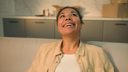 Happy relaxed African American woman female home owner joyful girl renter tenant sit on couch relax enjoy house renovation moving in new apartment relocation day buy rent real estate mortgage smileの写真素材