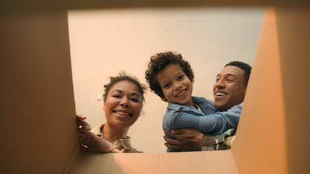 POV point of view open cardboard box looking inside African American happy family joyful parents son kid little boy child unpacking parcel delivery online shop receive package unboxing moving day homeの写真素材