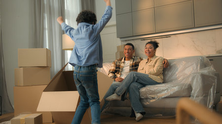 African American parents on home sofa family relocation moving day funny little son boy child play...