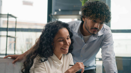 Indian businessman mentor coach help Arabian businesswoman with laptop teaching help explain online project paperwork two smiling multiracial woman and man business colleagues cooperate work in officeの写真素材