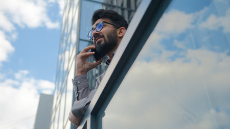 Bottom view Arabian businessman speak mobile phone outdoors on terrace serious Indian man talk with business partner smartphone call negotiate solve male CEO employer talking cellphone on city balconyの写真素材