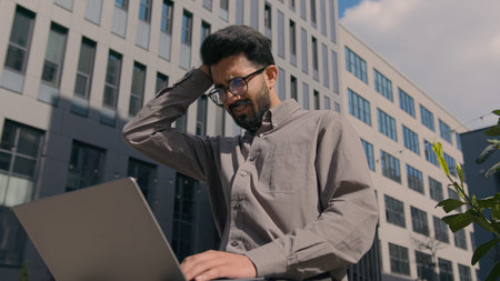 Arabian Indian businessman working on laptop in city outdoors worried man anxious male executive...