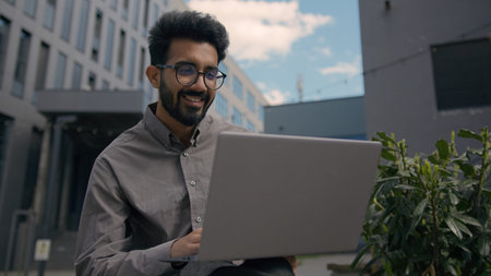 Moving shot Indian Arabian man smiling businessman employer entrepreneur working with laptop in city...