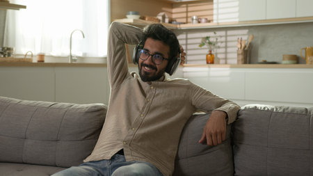 Relaxed happy man male relax on cozy sofa comfortable leisure satisfied guy wear wireless headphones turn on music listening song playing audio on mobile phoneの写真素材