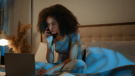 Angry African American woman businesswoman working on home bed with laptop papers mad talk mobile phone conflict stressed girl late night overwork problem with documents smartphone screaming arguingの写真素材