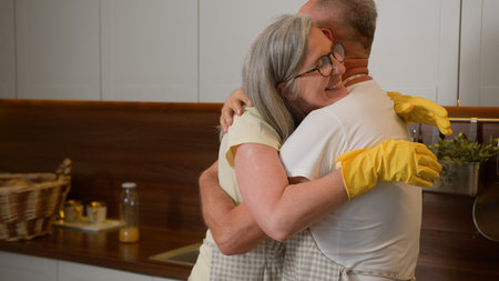Mature wife dancing with middle-aged husband old retired couple in love having fun listen music funny dance together in kitchen washing dishes household chores romantic relationship hugging cuddlingの写真素材