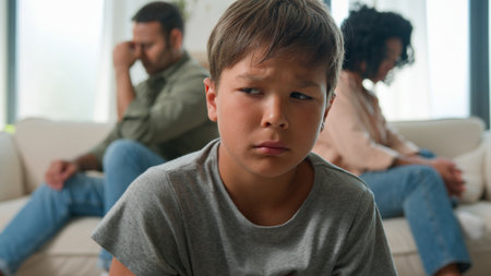 Multiracial diverse family annoyed married couple after quarrel sit separated on home sofa upset sad little boy kid son offended at parents psychological child trauma breakup mom dad conflict divorceの写真素材