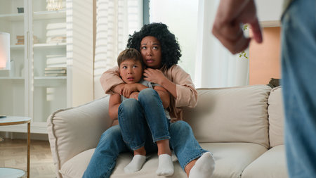 Domestic violence abuse in multiracial family scared woman protect kid child from aggressive drunk man with clenched fist home conflict fight attack menace threat afraid wife and son hide from husbandの写真素材