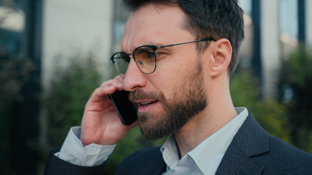 Caucasian businessman successful business entrepreneur commercial ceo employer chief walking on street talking mobile phone on way to work male busy man call cellphone speaking smartphone go outdoorsの写真素材