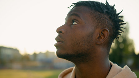 Outdoor close-up male face African American ethnic sport man pensive upset sad displeased frustrated guy looking up in sunbeam relax dream rest after workout breathe fresh air morning sunlight in cityの写真素材