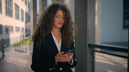 Smiling Caucasian woman business girl walking city street with smartphone young businesswoman call to colleague mobile conversation female employer lady talking phone communication outdoors downtownの写真素材