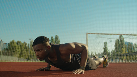 Athletic bodybuilder African American sportsman young man doing push-up exercise on football stadium...