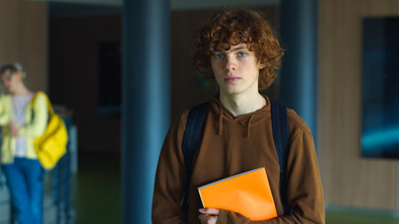 High school university teenager education study calm holding book posing in corridor alone serious Caucasian guy boy pupil teen male man schoolboy student studying learning college looking at cameraの写真素材