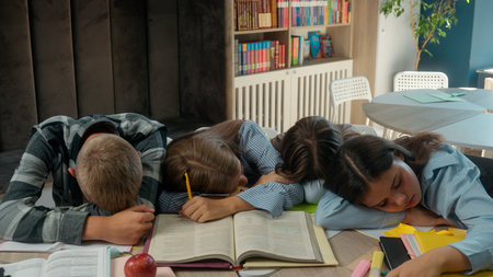 Caucasian four friends pupils tired exhausted fatigued students teens and teenagers boy guy male girls female at school library class sleeping napping on table books sleep together studying educationの写真素材