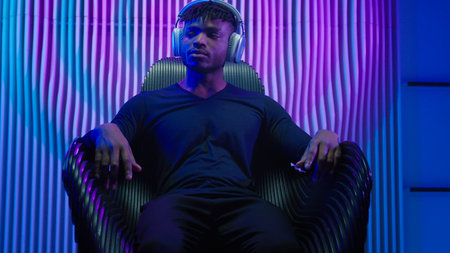 African American man guy male sitting in chair relaxing rest calm peace listen DJ mix listening audio song sound music in modern wireless headphones indoors neon light modern cyberspace innovationの写真素材