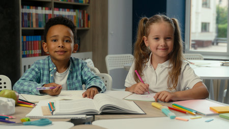 Cute little children multiethnic kids African boy Caucasian girl school pupils students classmates friends schoolboy schoolgirl in class together studying learning education smiling write draw at deskの写真素材