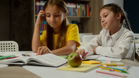 Sad little girls school education problem difficult task learn at classroom tired upset pupils students teens schoolgirls kids sisters children worried studying lesson reading book frustrated burnoutの写真素材