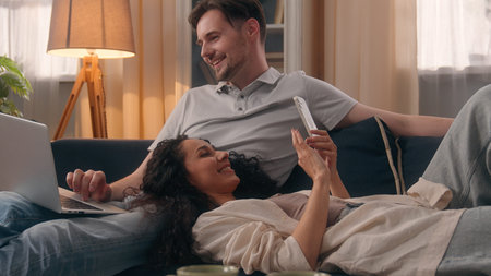 Couple using laptop and smartphone together at home on the couch, relaxing and bonding.