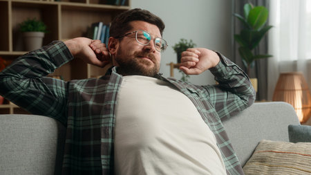 Smiling lazy relaxing resting Caucasian man guy male homeowner relax at couch sofa own rent home loan mortgage yawning stretching hands sleepy napping yawn sleep calm weekend indoors smile insomniaの写真素材