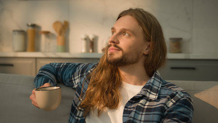 Calm relaxed man guy relaxing resting at new rental home apartment kitchen tranquil drinking organic black green tea drink coffee holding cup beverage thinking relaxの写真素材