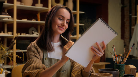 Caucasian woman girl artist painting notebook sketch drawing female designer sculptor potter artwork in studio creative handmade workshop pottery art class craft design paint ceramics modeling clayの写真素材