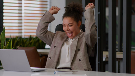 Happy African American woman girl ethnic businesswoman business lady joyful worker employee at office workplace online work laptop computer email good news win dance celebrate offerの写真素材