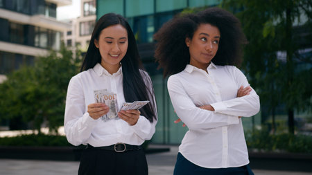 Asian Korean African American women count money salary bonus income envy arms crossed females inequality business financial colleague rivalry jealousy cash pay bills discrimination girls rich outdoorsの写真素材