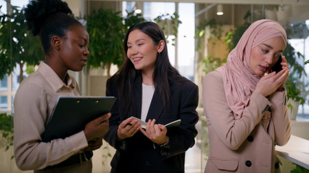 Diverse multiethnic girls three women female teamwork at office African Asian businesswomen business partners three happy smiling cheerful happy co-workers conversation Muslim colleague talking phoneの写真素材