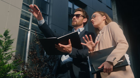 Two stylish businesspeople colleagues wearing sunglasses talking in city outside office discuss startup project papers documents businessman communicate with businesswoman business man woman teamworkの写真素材