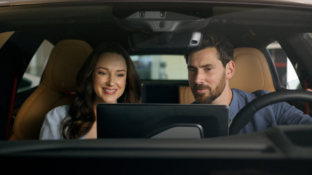 Happy couple sitting inside new luxury modern electric car choosing automobile looking around married Caucasian man with woman choosing auto in salon discuss talking smiling rent service credit buyingの写真素材