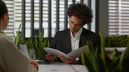 Two diversity business multiracial men businessmen in office talking papers documents research teamwork intern male guy interview hiring work African American boss reading resume insurance tradingの写真素材