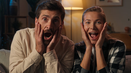 Caucasian woman man shocked surprised family husband wife couple looking at camera evening night at home positive millennials shock open mouth surprise wonder amazing good news wow emotions excitedの写真素材
