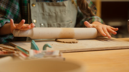 Talented creative teenage Caucasian little girl artist sculptor child ceramist kid student use wooden rolling pin rolls clay material preparing craft artwork sculpture ceramic pottery indoor workshopの写真素材