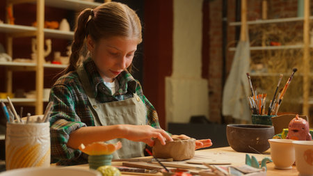 Happy Caucasian teenager little girl school child kid daughter schoolgirl student pupil potter artisan creating clay ceramic bowl vase creation craft activity using tools inside pottery class workshopの写真素材