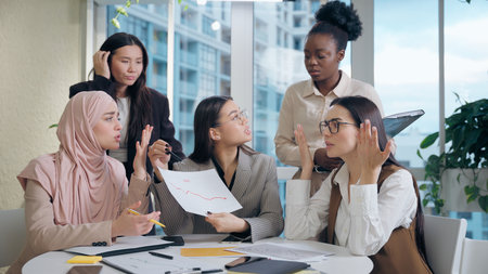 Stressed frustrated multiethnic women females team girls African American Caucasian Japanese Muslim hijab Arabian businesswomen argue business conflict low graph stress analyze document inside officeの写真素材