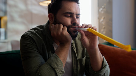 Lonely sad upset depressed Caucasian European model despair man male guy homeowner businessman in festive cap on head blowing in whistle celebrating birthday alone single depression indoor home roomの写真素材