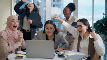 Excited shocked multiethnic women females businesswomen team colleagues multiracial group looking laptop computer celebrating win shock business offer deal success applause indoor office meeting roomの写真素材