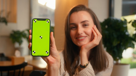 Caucasian happy smiling joyful woman female girl typing drinking coffee croissant client visitor in cafe indoors holding mobile phone showing green screen online menu service chroma key display appの写真素材