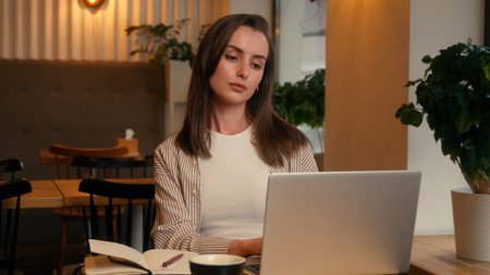 Business woman in cafe working laptop writing notes businesswoman in cafeteria with computer online task female girl journalist author work job freelance at table concentrated focused write ideasの写真素材