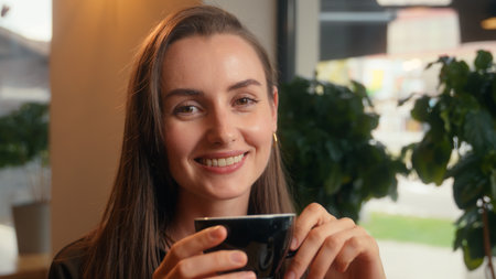 Happy smiling relaxed Caucasian woman girl female business businesswoman lady indoors in cafe in cafeteria restaurant drinking aroma coffee tea drink beverage breakfast lunch croissant smile at cameraの写真素材