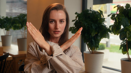 Portrait negative Caucasian woman crossed hands no not stop reject gesture sitting in cafe businesswoman female business girl looking at camera answer disagree deny keep distance protect crossing armsの写真素材