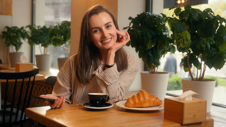Smiling happy woman girl cafe visitor client in cafeteria restaurant female holding mobile phone showing green screen smartphone display mock up chroma key screen website menu order smile at cameraの写真素材