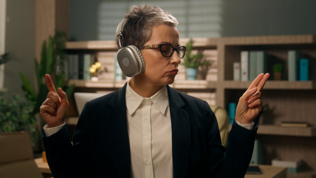 Relaxed having fun work pause freedom Caucasian senior business woman middle-aged businesswoman adult mature female employer in office listening music in wireless headphones enjoy audio song dancingの写真素材