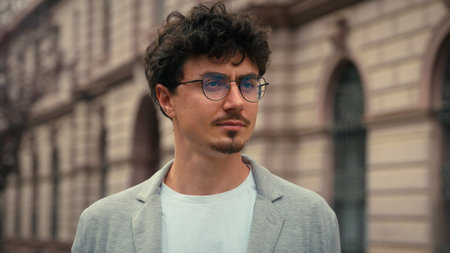 Close up portrait handsome European millennial pensive serious calm 30s guy in glasses looking around standing in city stylish business man confident businessman male outdoors travel posing at streetの写真素材