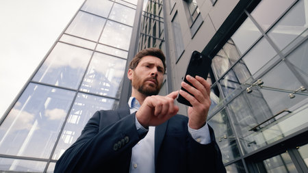 Serious worry anxiety professional male near office building company looking around problem lost in city Wi-Fi connection confused Caucasian man business guy businessman using typing mobile phoneの写真素材