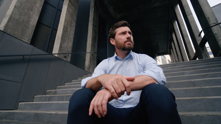 Stressed upset annoyed despair suffering fired unemployed Caucasian middle-aged businessman sitting on company office stairs outside burnout overworked business man male guy in city dismissal lost jobの写真素材