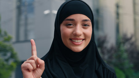 Portrait happy smiling Muslim business woman Islamic businesswoman girl female in black hijab employer in city showing one finger come up with idea solution decision pensive dreaming thinking outdoorsの写真素材