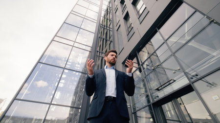 Caucasian worried businessman lost in city near office building anxiety looking cellphone screen business man male guy employer using mobile phone GPS navigator app online smartphone chat bottom viewの写真素材